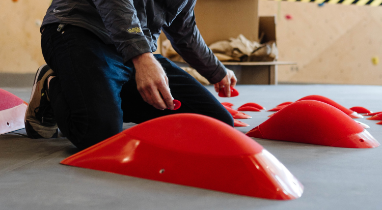 A routesetter kneeling in front of red climbing holds.